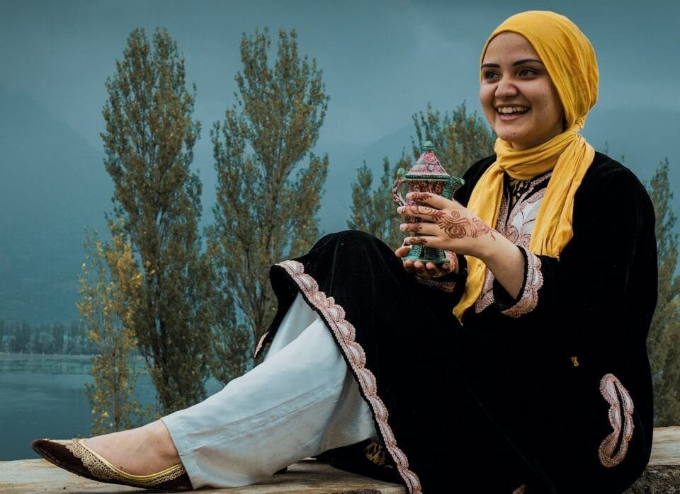 woman in black jacket and white hijab sitting on brown wooden log during daytime
